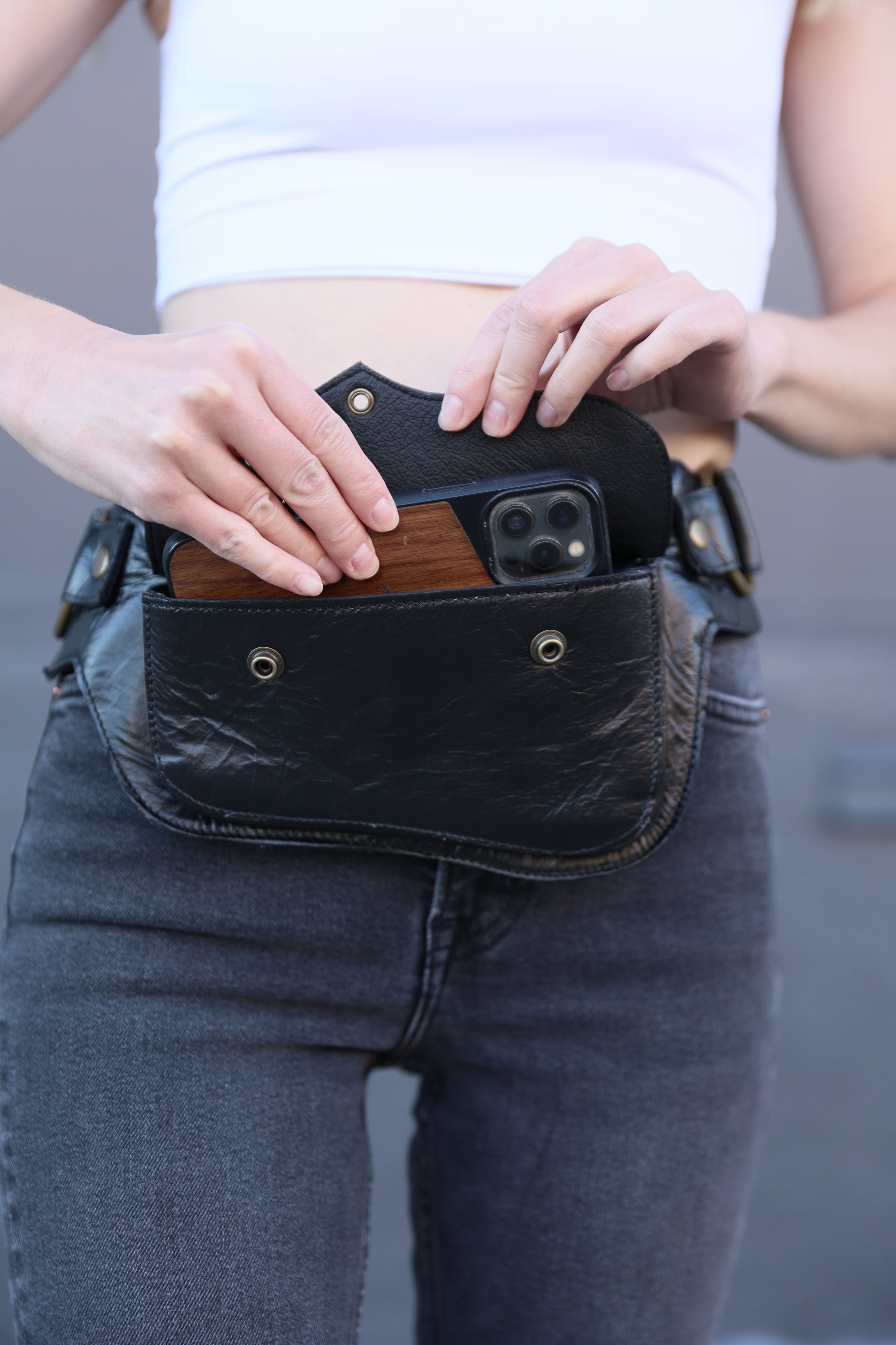 Person putting a large phone in a leather fanny pack 