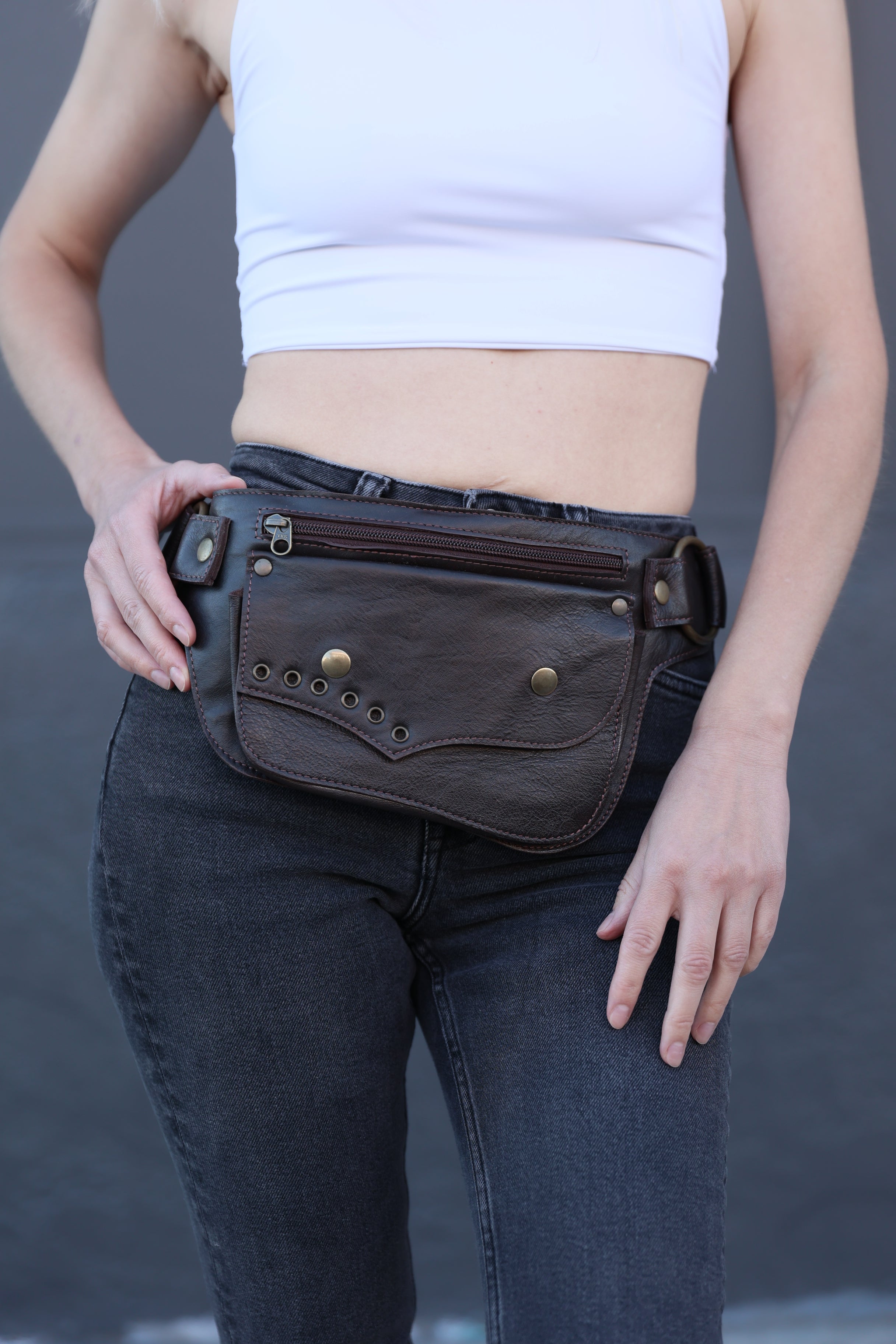 Person holding a brown leather bag with visible stitching and gold rivets against a neutral background