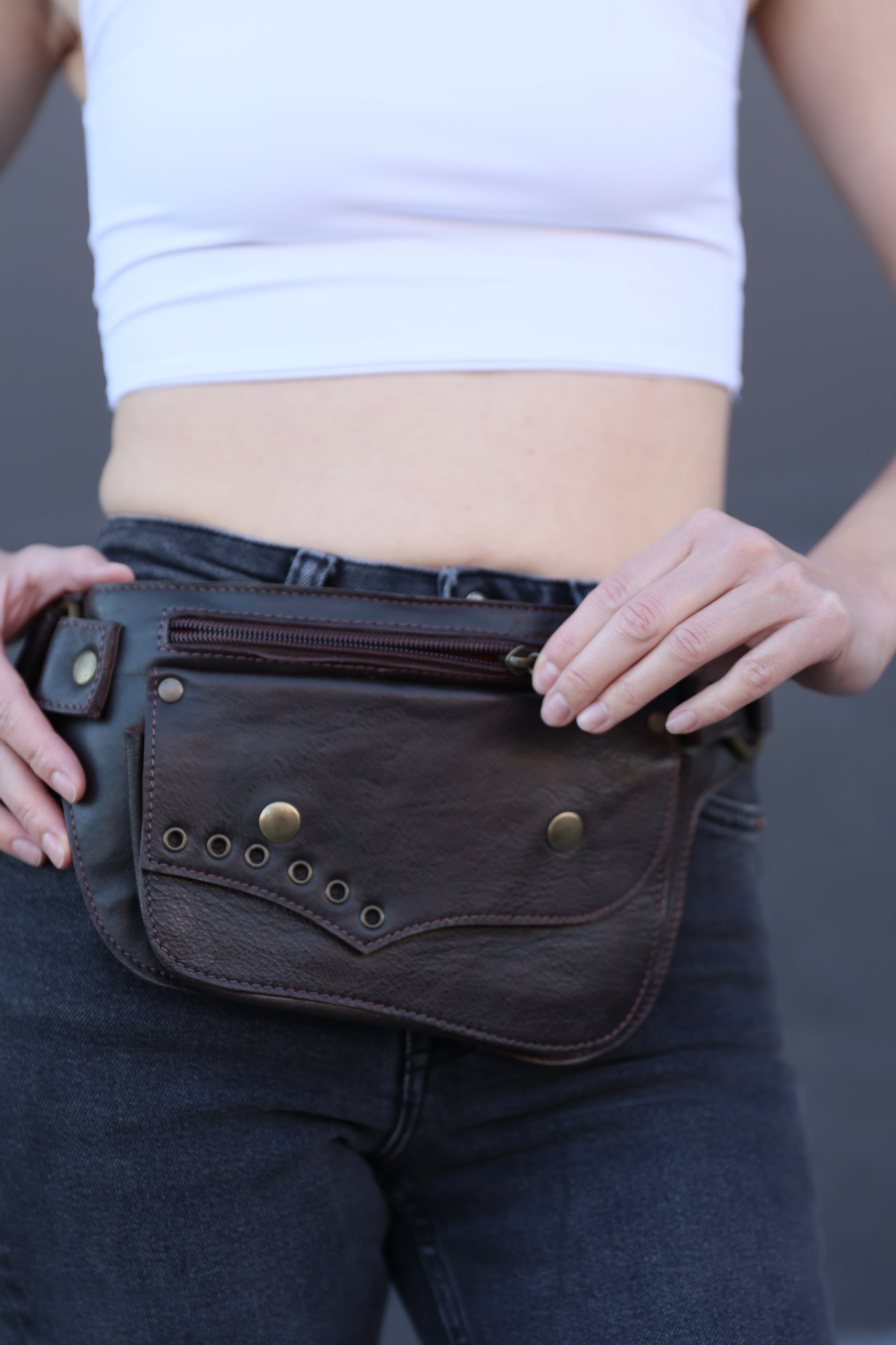 Person holding a brown leather bag with visible stitching and buttons.