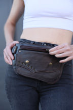 Person wearing a dark leather pouch around their hips against a neutral background