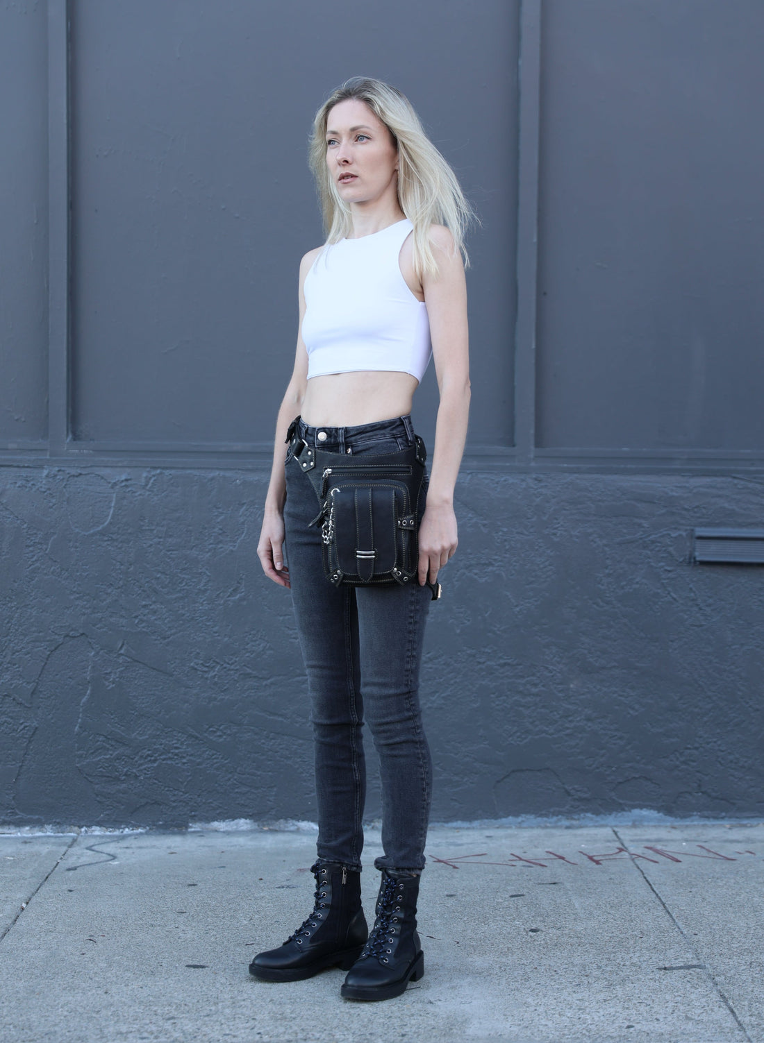 Person wearing black high-waisted jeans and black knee-high boots against a gray wall.