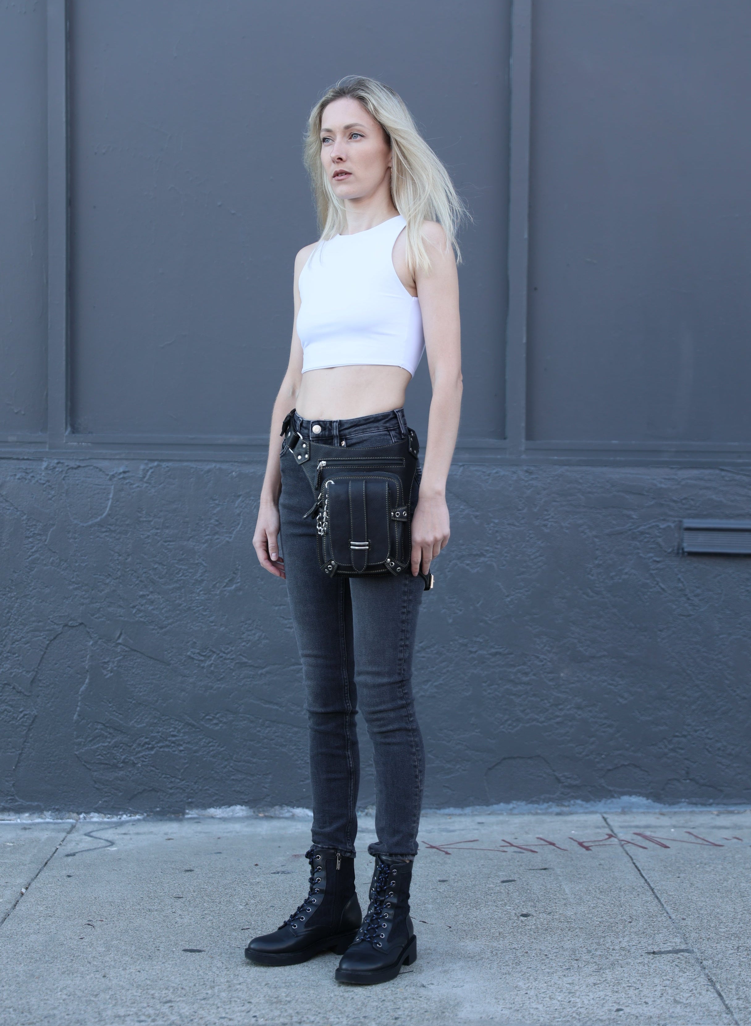 Person wearing black high-waisted jeans and black knee-high boots against a gray wall.