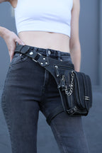 Person wearing a black leather waist bag with studs and chains on a gray background