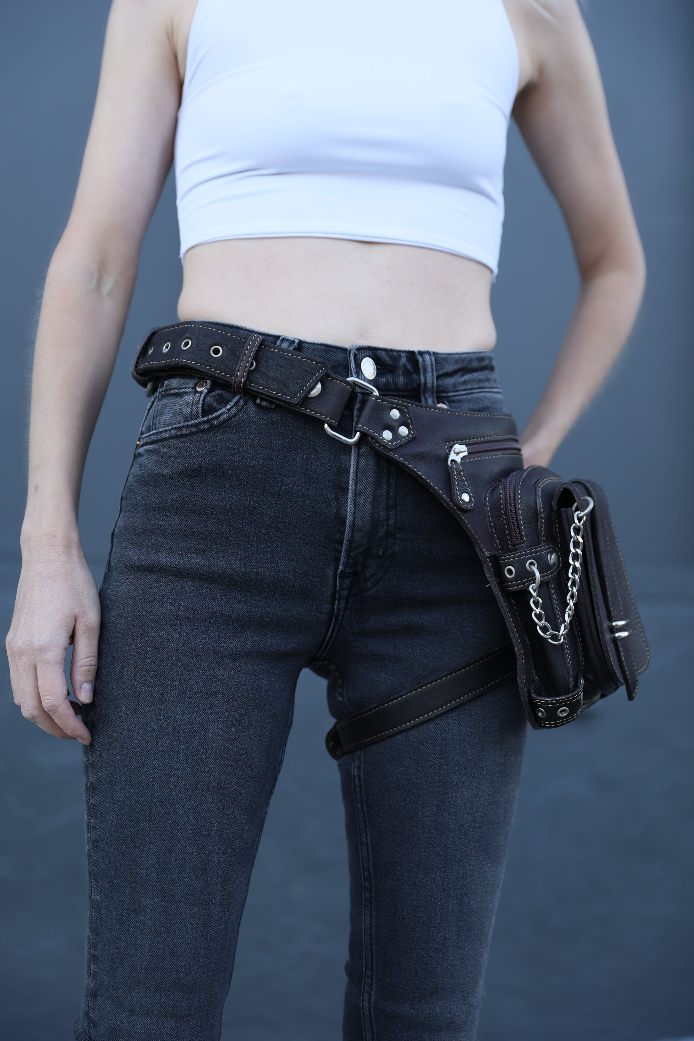 Person wearing black leather harness with silver hardware on a plain background
