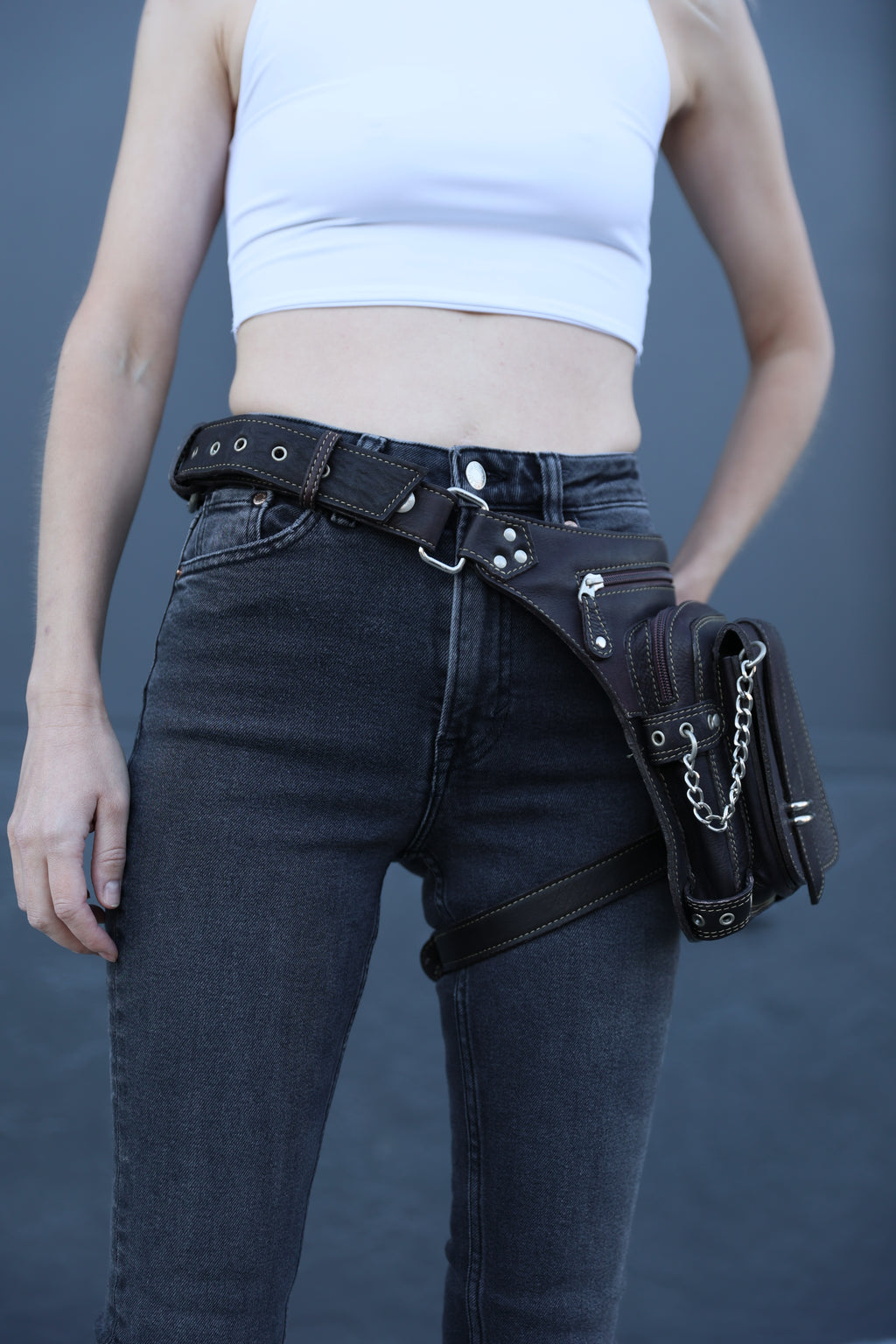 Person wearing black leather harness with silver hardware on a plain background