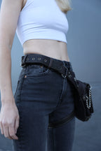 Person wearing black jeans with a unique belt design on a gray background