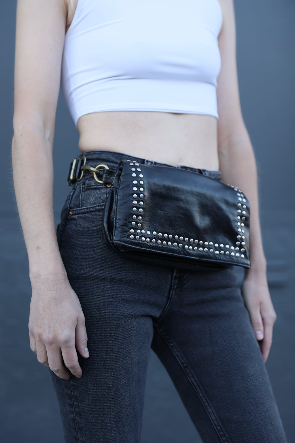Person wearing black jeans with studded details and a white top against a gray background