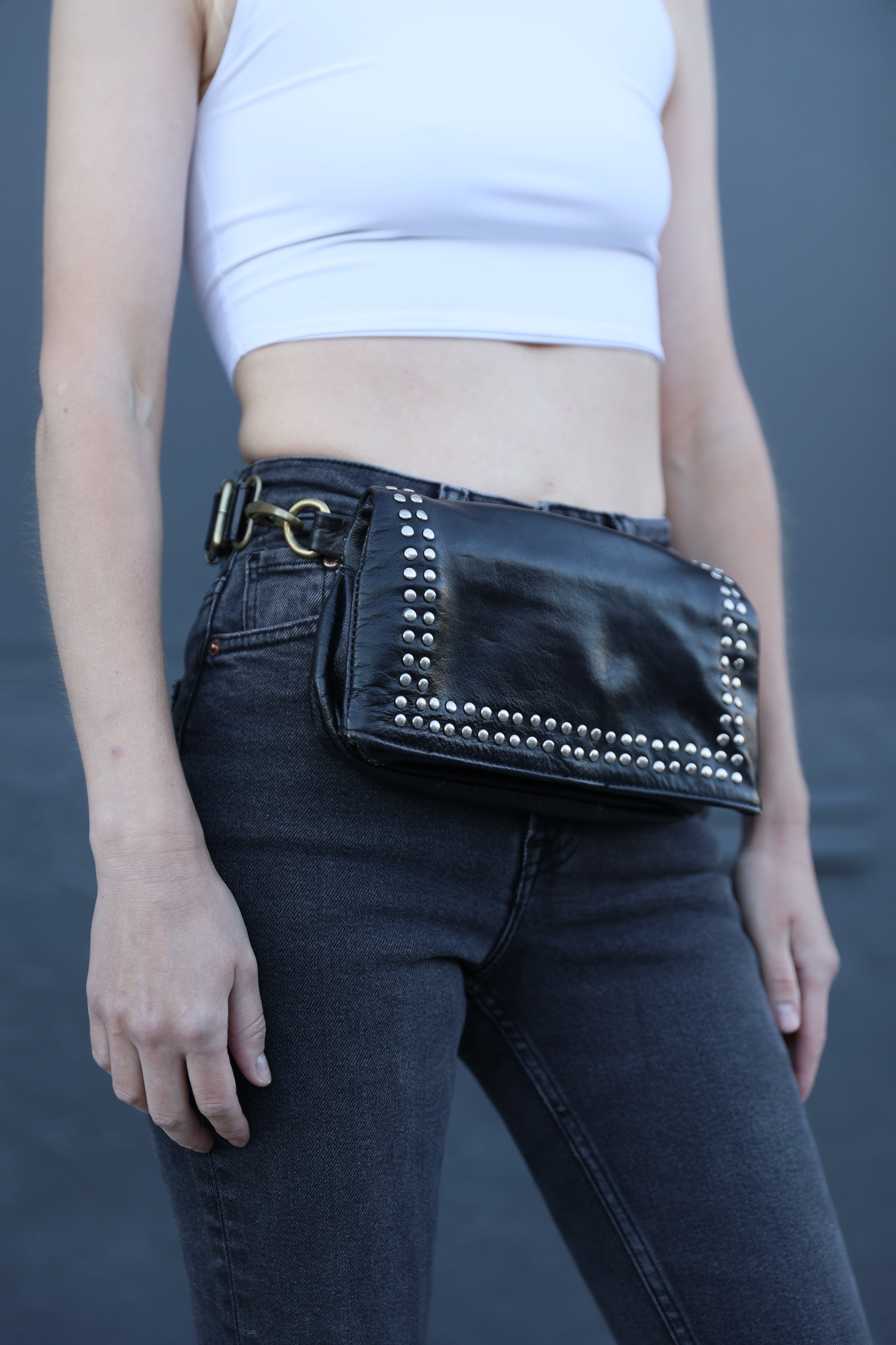 Person wearing black jeans with studded details and a white top against a gray background