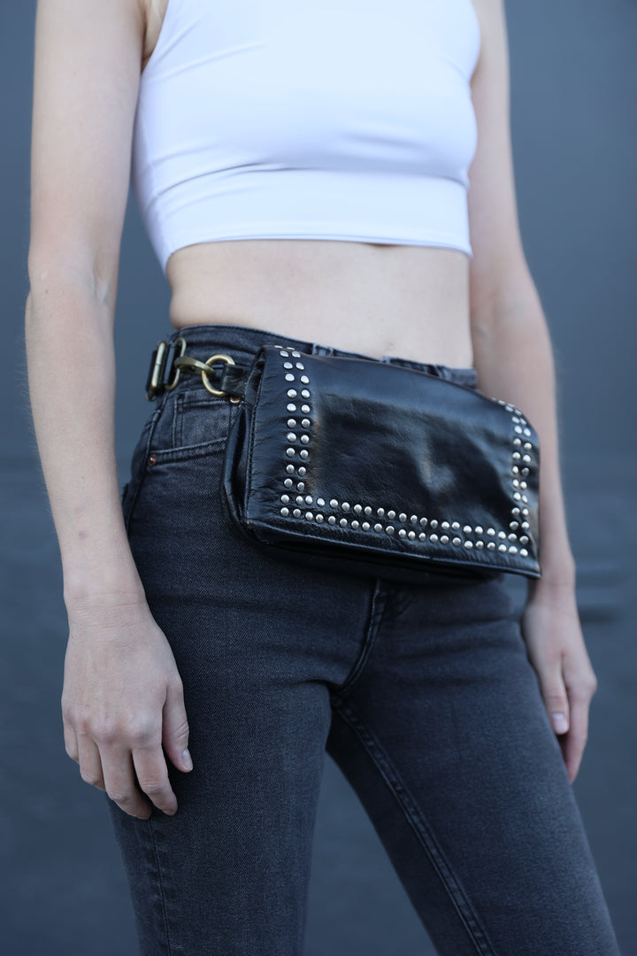 Person wearing black jeans with studded details and a white top against a gray background