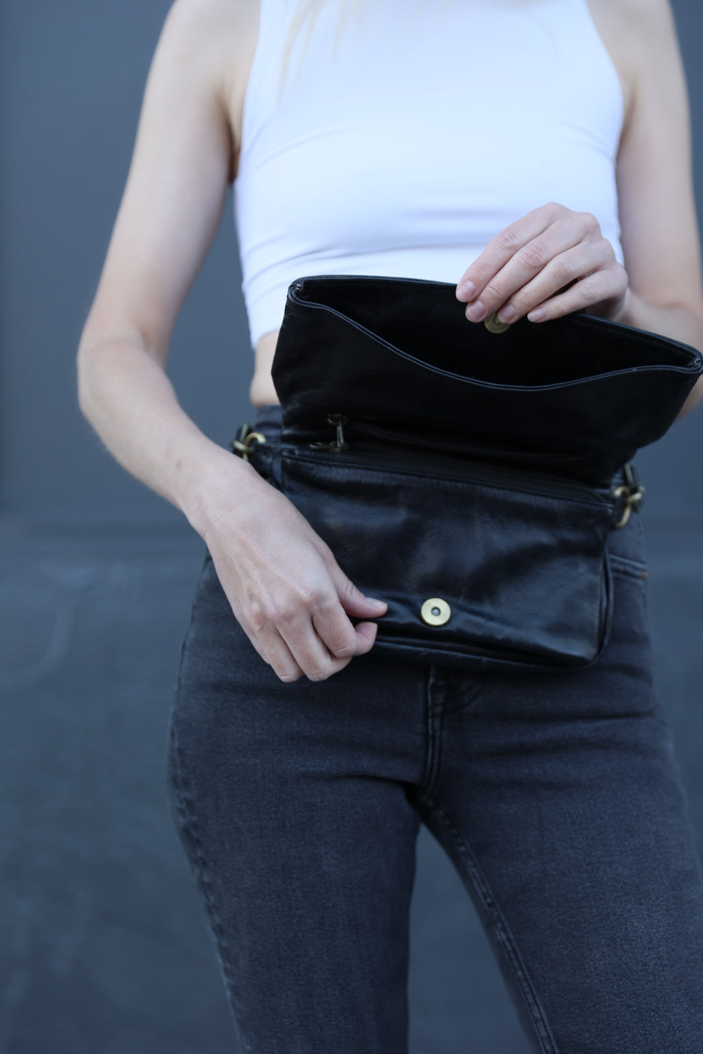 Person holding a black leather clutch bag with a neutral background