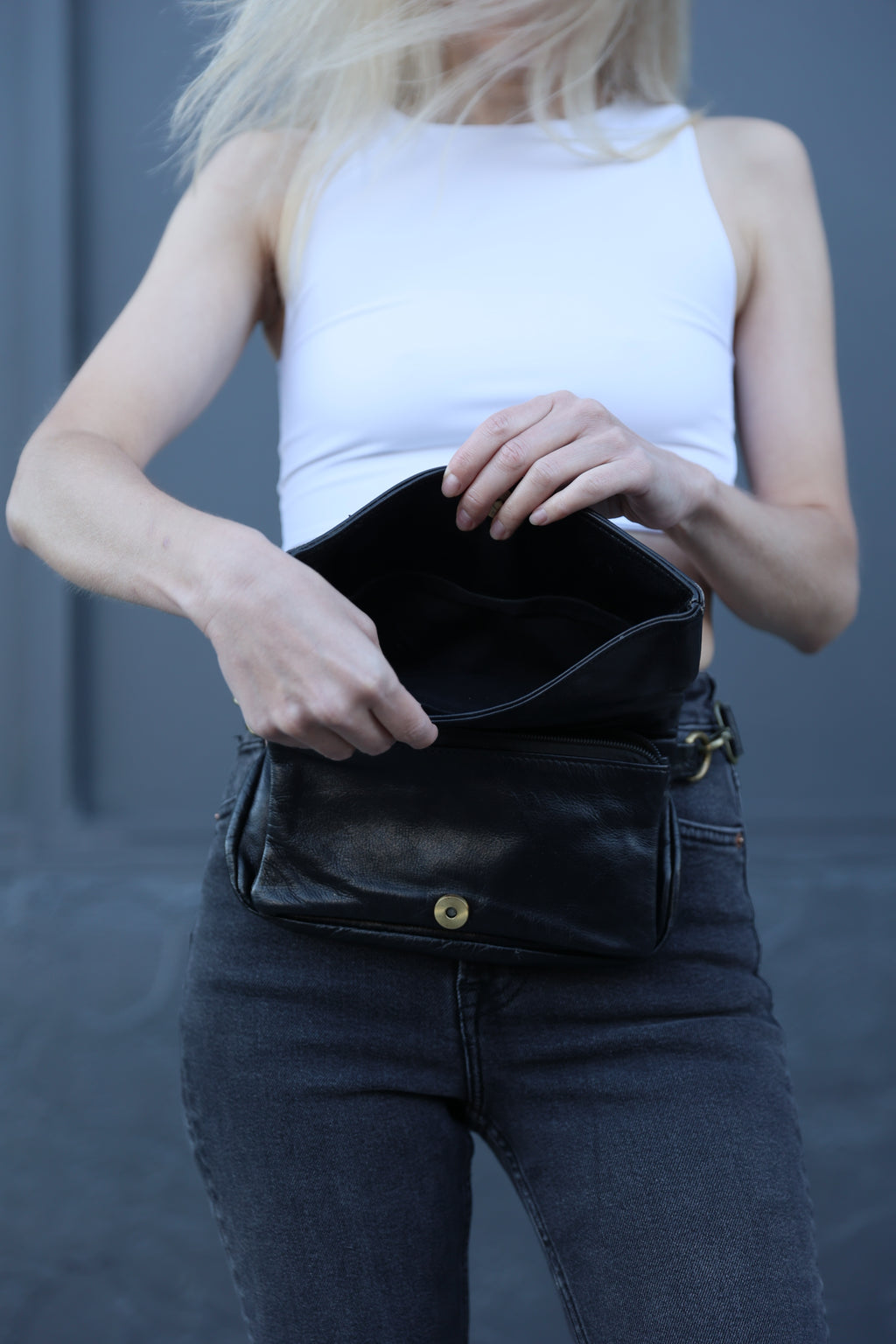 Person holding a black leather jacket against a gray background