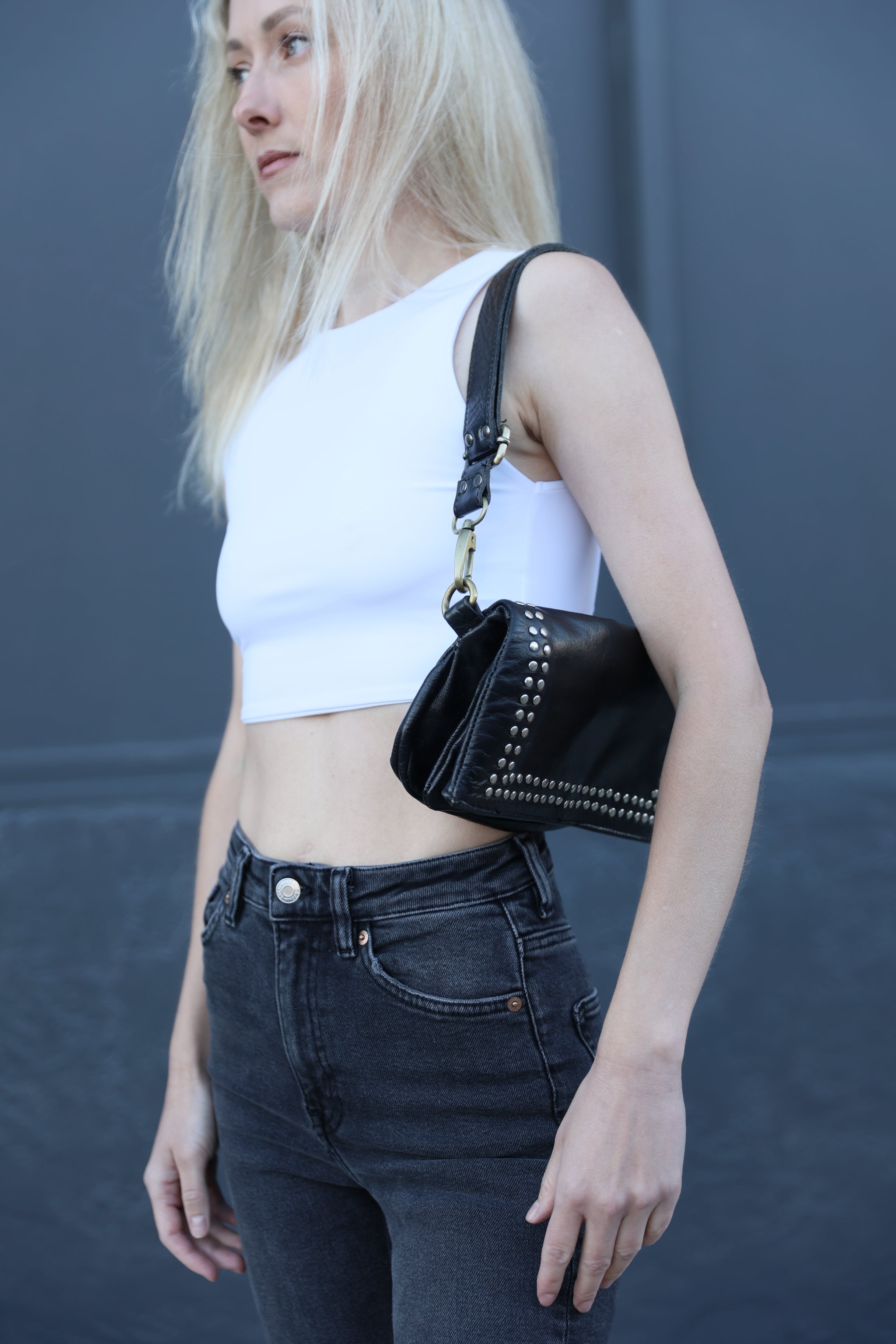 Person wearing a white top and black jeans with a black bag over their shoulder against a gray background