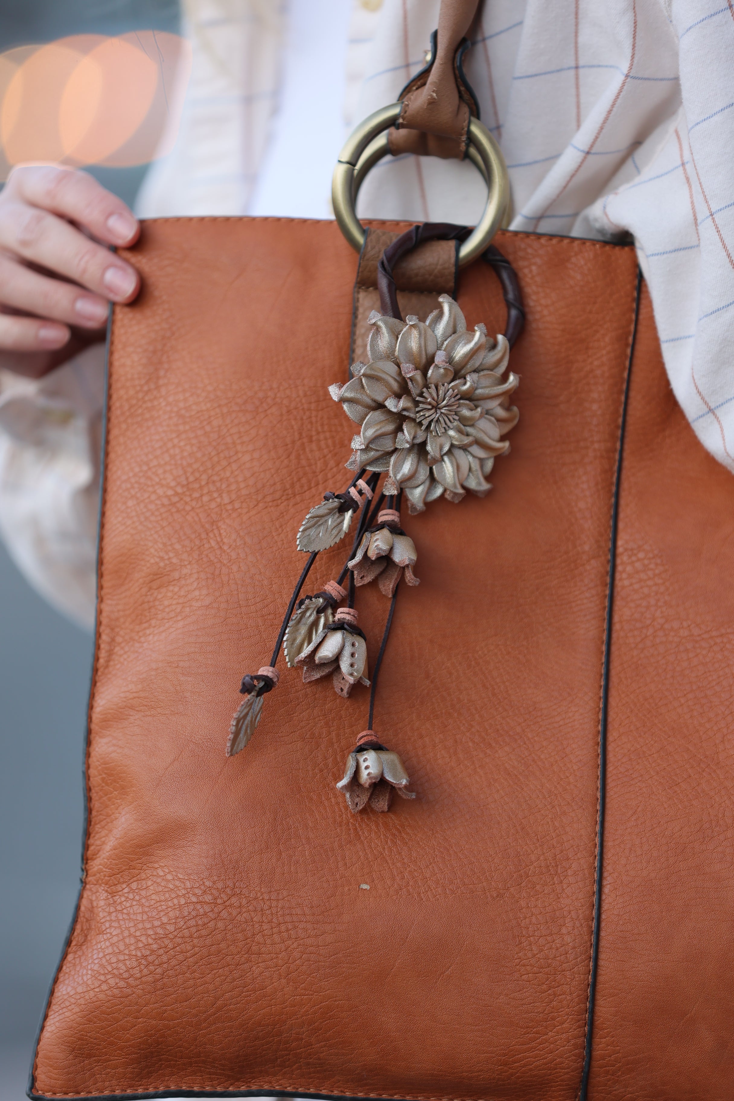 Brown leather clutch bag with floral embellishment held by a hand.