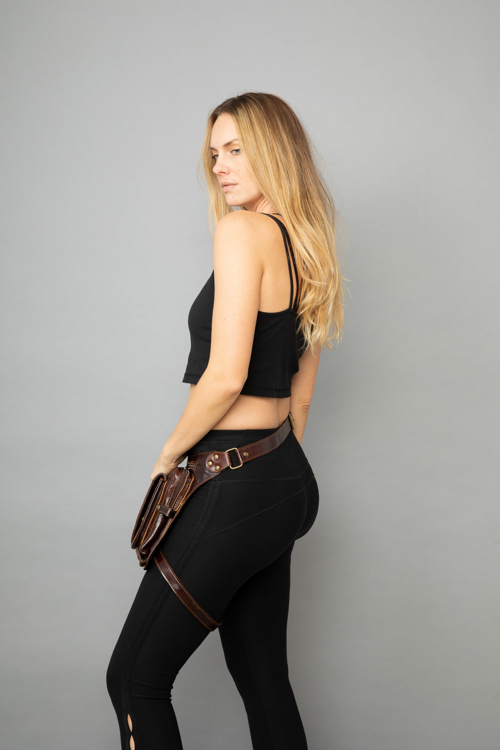 Woman wearing a black outfit with a brown belt on a gray background