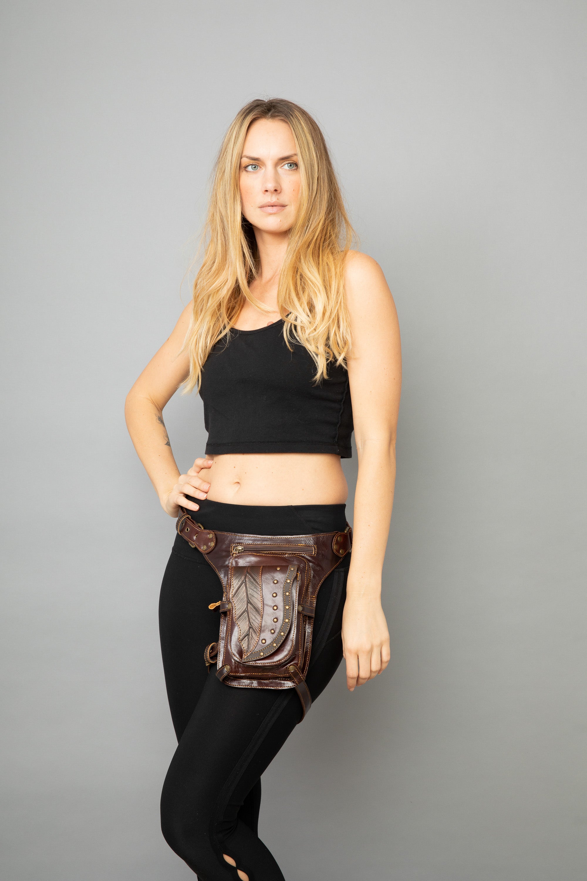 Woman wearing a black outfit with a brown leather belt bag on a gray background