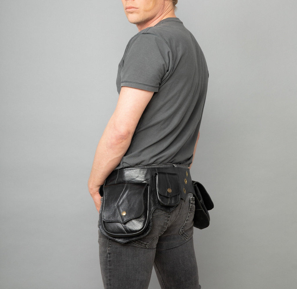 A man facing away from the camera is wearing a black leather utility belt with large side pouches and a small back pouch. He has a grey shirt and blue jeans on.