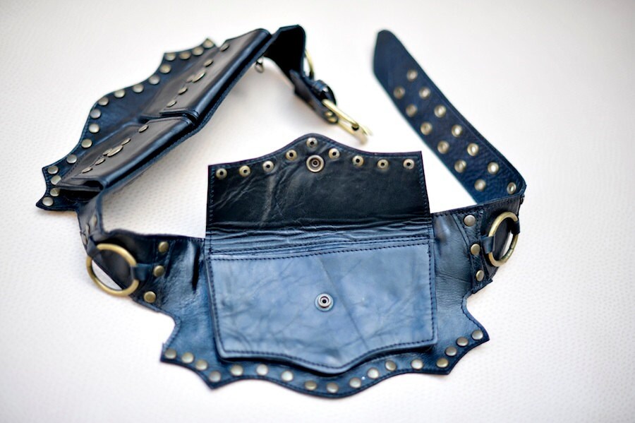 Close up of a black leather belt with an open large pouch against a beige background
