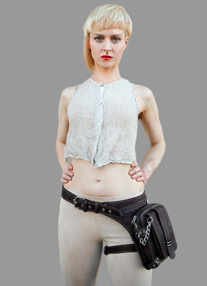 Woman wearing a white sleeveless top and beige pants with a black waist bag on a gray background